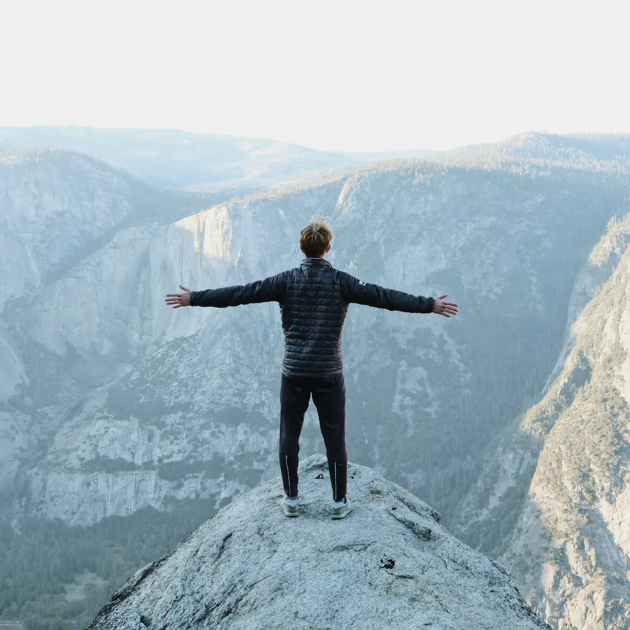 man opening his arms wide open on snow covered cliff with view of mountains during daytime